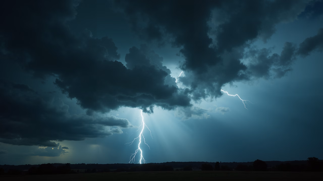 Dramatic thunderstorm with lightning illuminating dark clouds over a flat landscape.
