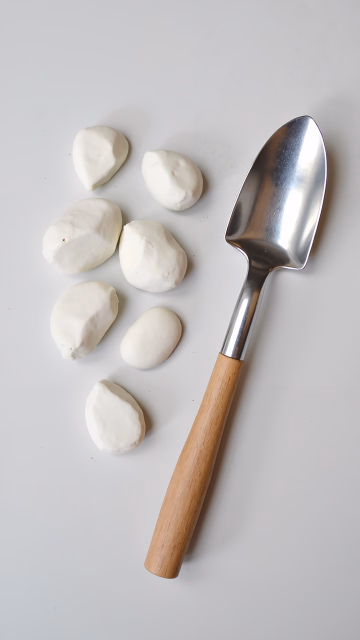 Minimalist still life with clay pebbles and a garden trowel on a white background.