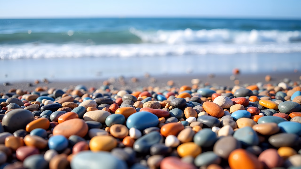 Vibrant pebbles on a sunny beach with ocean waves in the background.