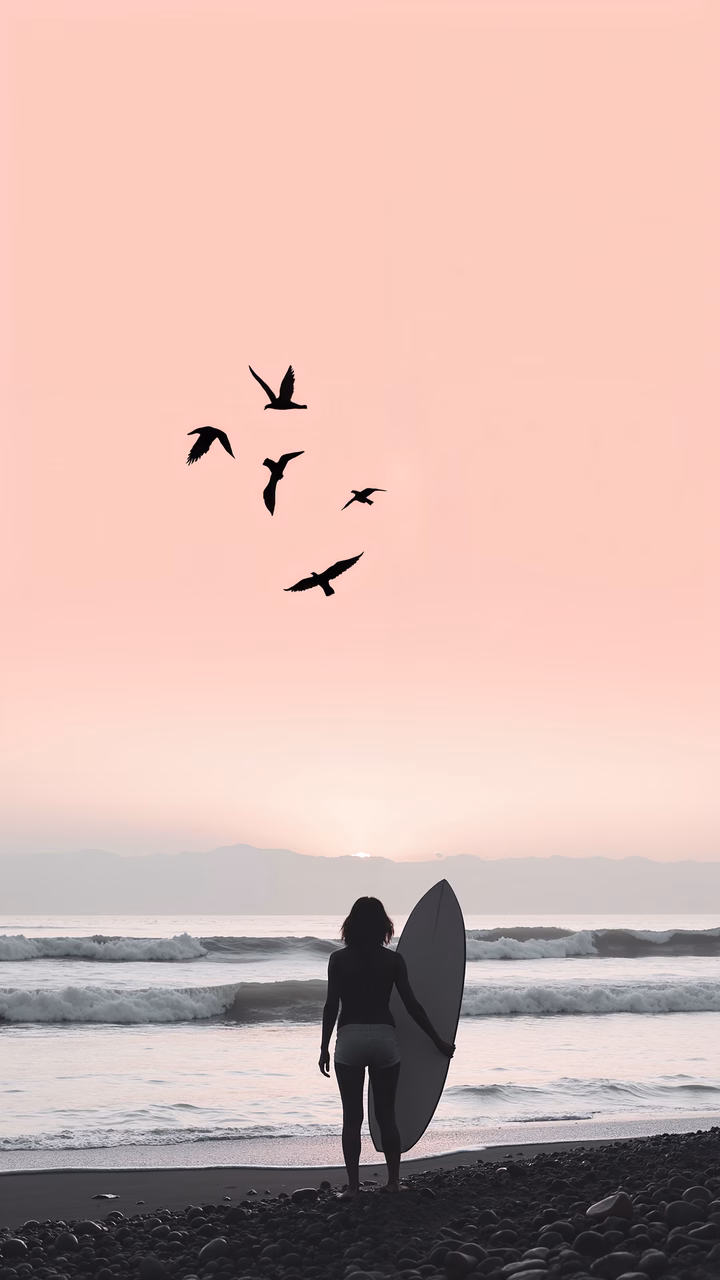 Silhouette of a surfer at sunset, with birds flying overhead, capturing a serene moment by the ocean.