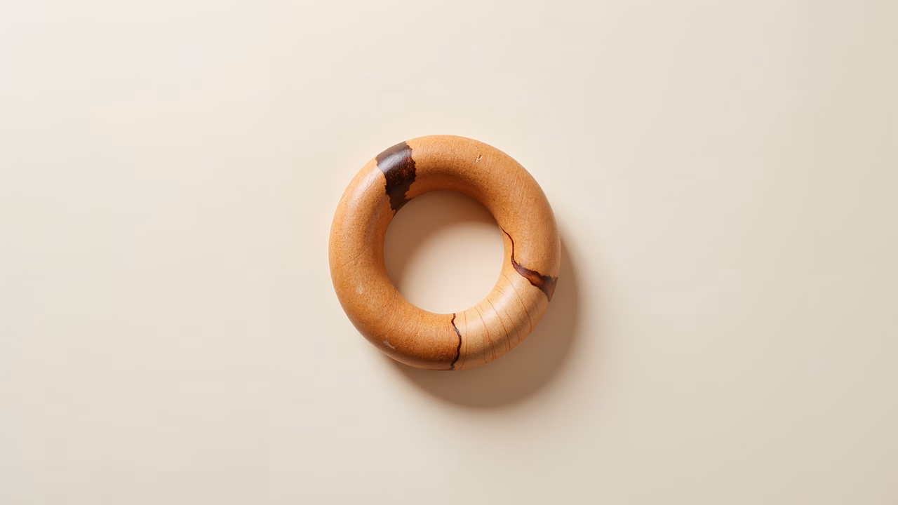 Close-up of a wooden ring with natural grain and knots on a beige background.