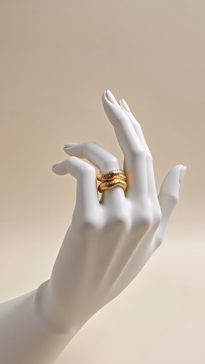 Close-up of elegant golden rings on a white hand against a neutral background.