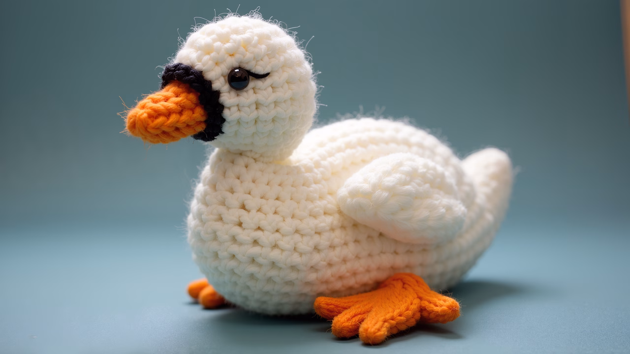 A delightful crocheted duck crafted with white and orange yarn, set against a teal backdrop.
