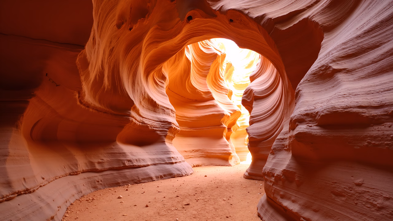 A stunning desert canyon with vibrant orange and red sandstone layers and bright light streaming through the opening.